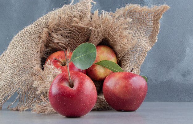 Свежие яблоки вываливаются из покрытой тканью корзины на мрамор.