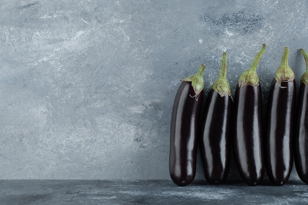 Free photo fresh aubergine row on grey background.