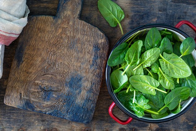 Fresh baby spinach leaves in a bowl on a rustic wooden table. Copy space