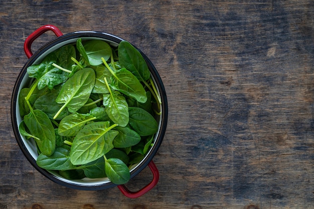 Fresh baby spinach leaves in a bowl on a rustic wooden table. Copy space