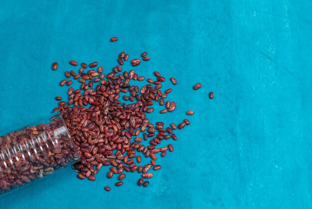 Fresh beans falling out of jar on a blue plaster surface