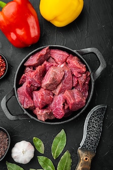 신선한 쇠고기 덩어리는 달콤한 피망, 주철 프라이팬, 검은색 돌 배경, 위쪽 전망 플랫 레이와 함께 요리할 수 있는 재료와 함께 테이블에 제공됩니다.