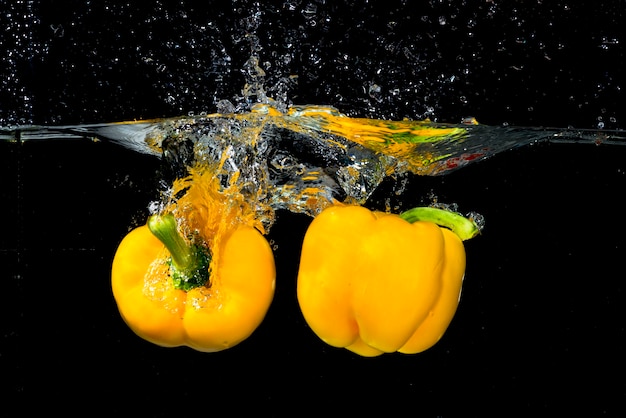 Fresh bell peppers falling in water against black background