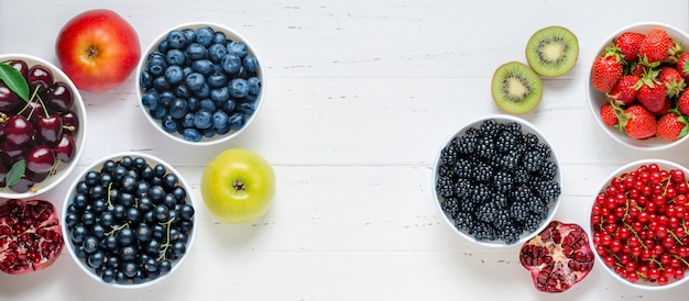 Свежие ягоды, фрукты, орехи на белом фоне деревянных. концепция здорового питания. пища содержит витамины и микроэлементы. скопируйте пространство.