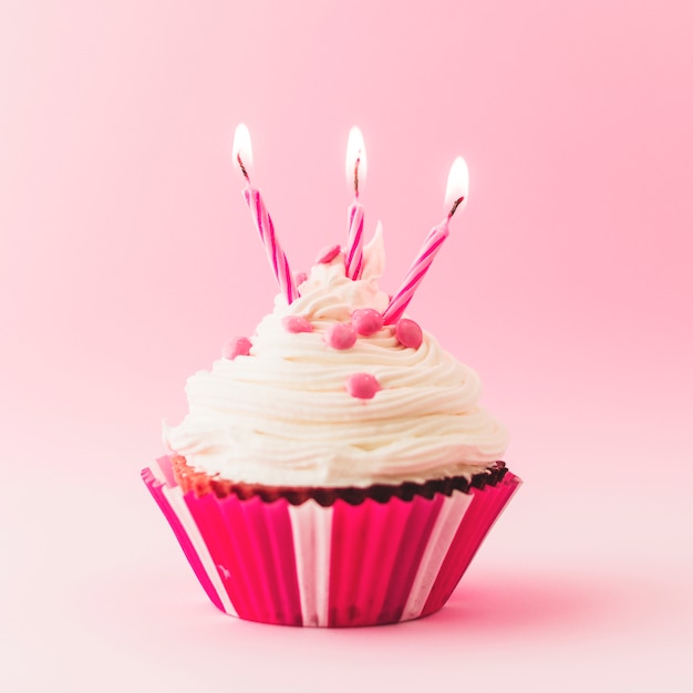 Fresh birthday cupcake with burning candles on pink backdrop