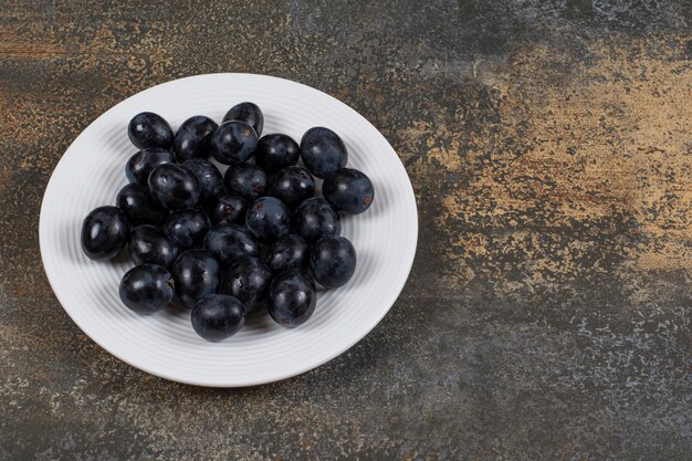 Fresh black grapes on white plate.