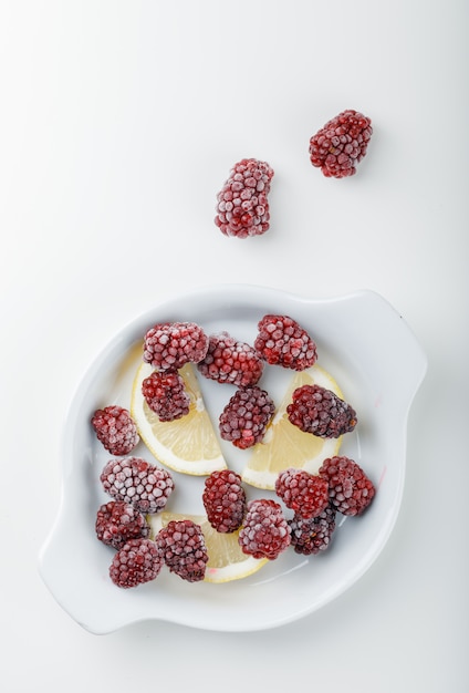 Free photo fresh blackberries in a white plate with lemon slices top view