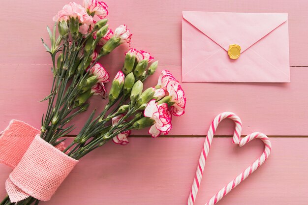 Свежий букет цветов с лентой возле конверта и леденцы