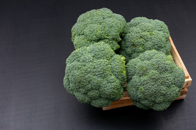 Fresh broccoli in wooden box on black surface green vegetables