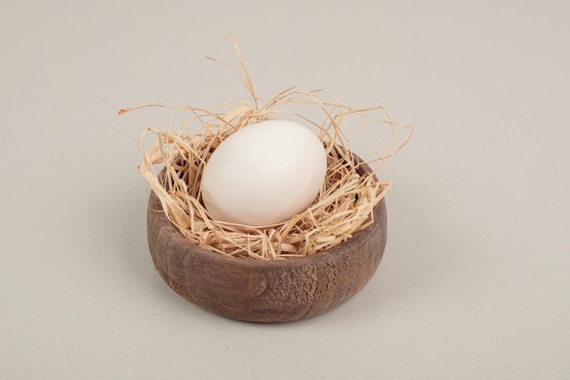 木製のボウルに干し草と新鮮な鶏の白い卵。