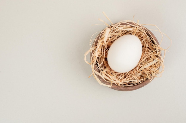 Free photo fresh chicken white egg with hay in wooden bowl.