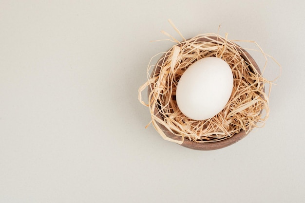 Fresh chicken white egg with hay in wooden bowl.