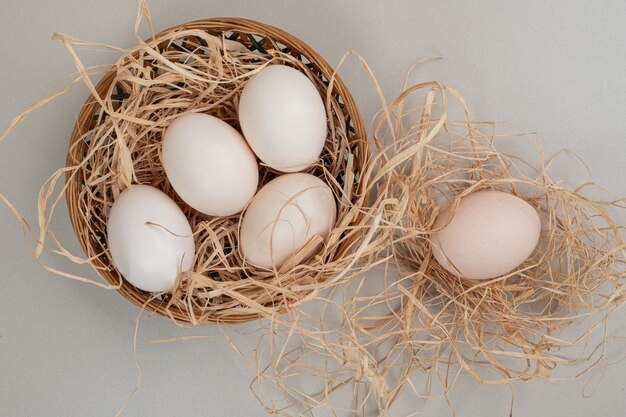 Fresh chicken white eggs with hay on wicker basket .