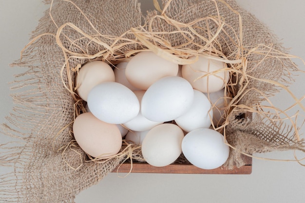 Fresh chicken white eggs with hay on wooden basket .