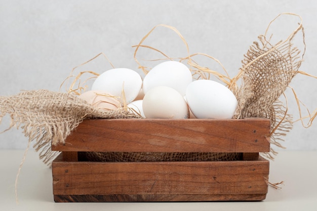 Fresh chicken white eggs with hay on wooden basket .