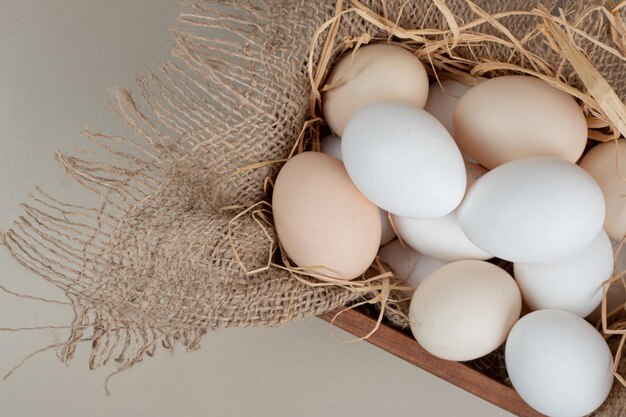 Fresh chicken white eggs with hay on wooden basket .