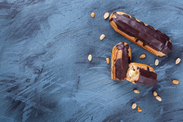 Fresh chocolate eclairs and peanuts placed on blue background. 