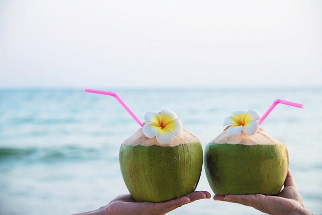 Fresh coconut in couple hands with plumeria decorated on beach with sea wave - honeymoon couple tourist with fresh fruit and sea sand sun vacation concept