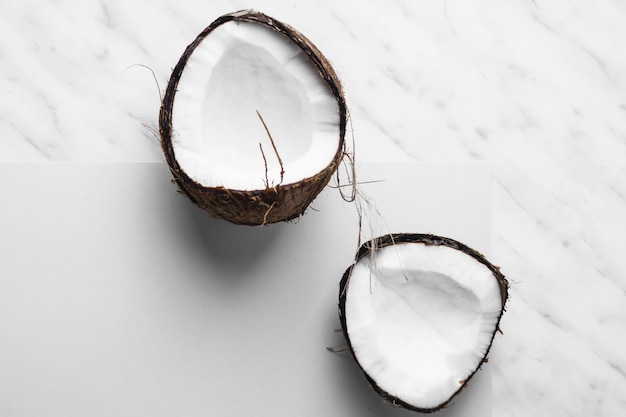 Fresh coconut cut in half on white and marble backdrop