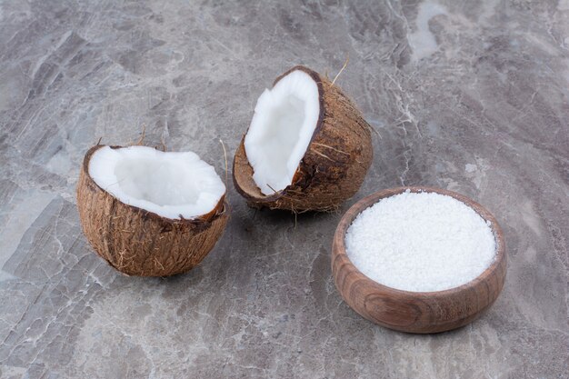 Fresh coconuts and bowl of sugar on stone surface. 