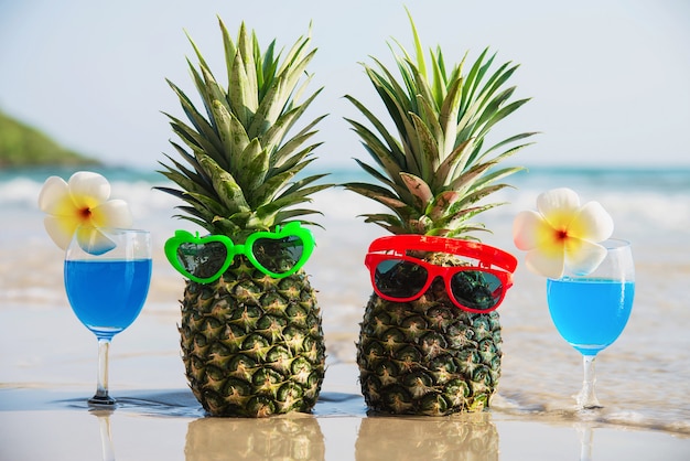 Fresh couple pineapples with sun glasses and cocktail glasses on clean sand beach with sea wave - fresh fruit and drink with sea sand sun vacation concept