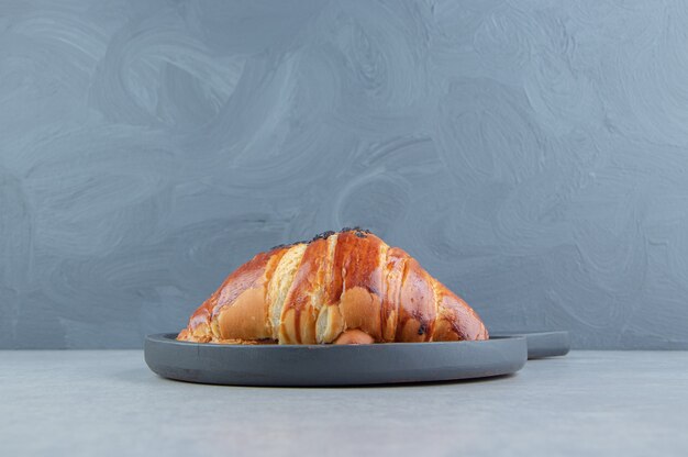 Fresh croissant decorated with drop chocolate on black board. 