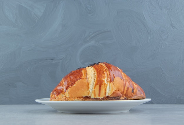 Fresh croissant decorated with drop chocolate on white plate. 