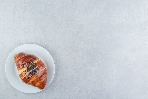 Fresh croissant decorated with drop chocolate on white plate. 