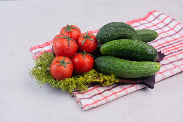 Fresh cucumbers, tomatoes and greens on tablecloth