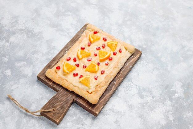 Fresh delicious puff pastry with pomegranate seeds and orange slices on concrete 