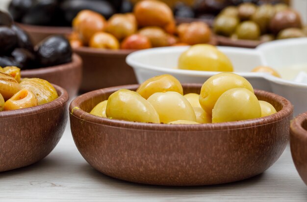 Fresh and different olives in a clay and white bowls on white wood. side view.