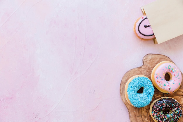 Free photo fresh donuts on chopping board near package over pink background