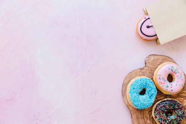 Fresh donuts on chopping board near package over pink background