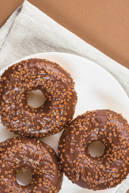 Fresh donuts with chocolate coating and sprinkles on plate