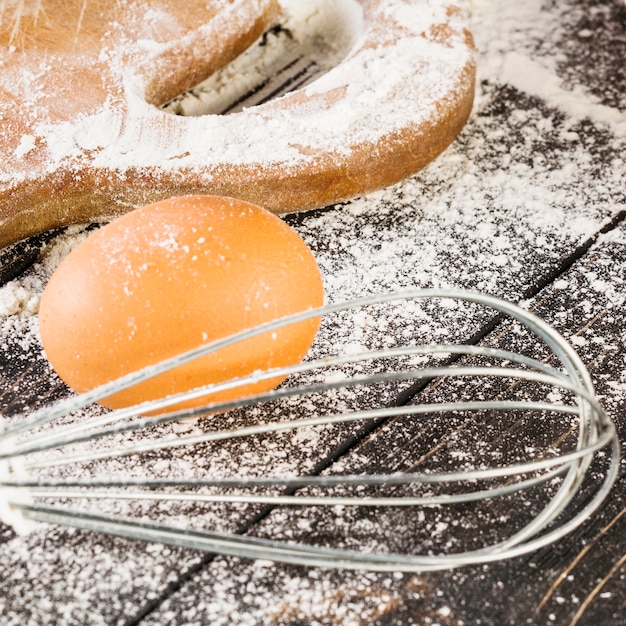 Fresh egg and wheat flour with whisker on wooden table