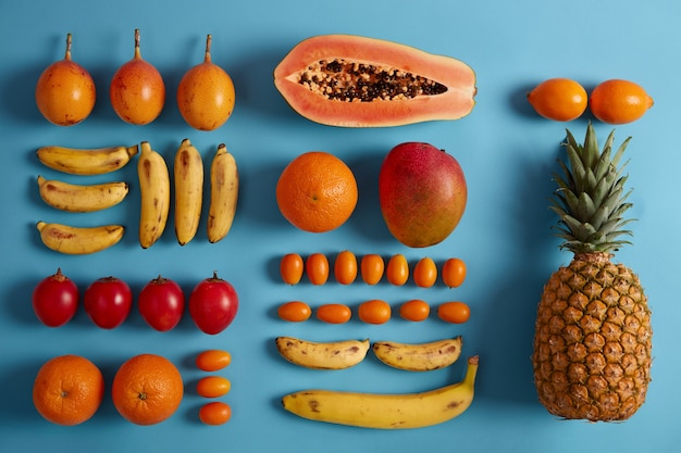 Fresh exotic fruits on blue background. Pineapple, papaya, bananas, cumquat, fortunella, source of vitamins. Summer tropcial composition. Fruits for making juice or smoothie. Food concept. Flat lay