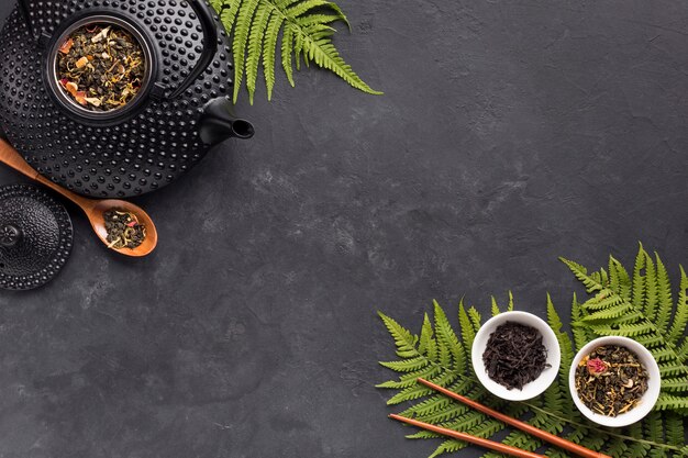 Fresh fern leaves and tea herb with black teapot on black slate background