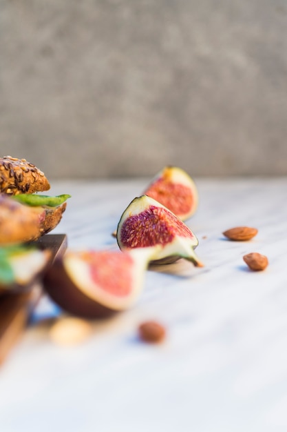 Fresh fig slices and almonds near hot dog on wooden board over white background