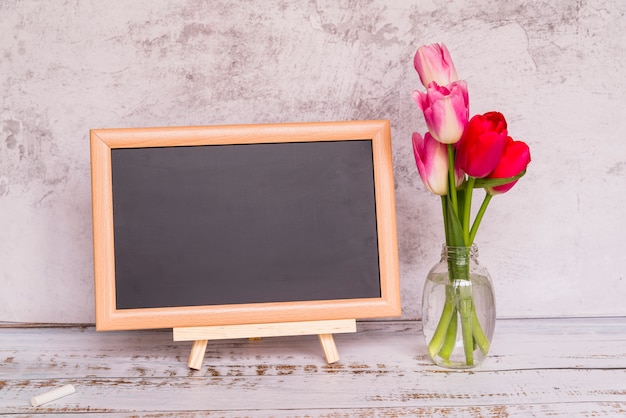 Fresh flowers on stems in vase and chalkboard