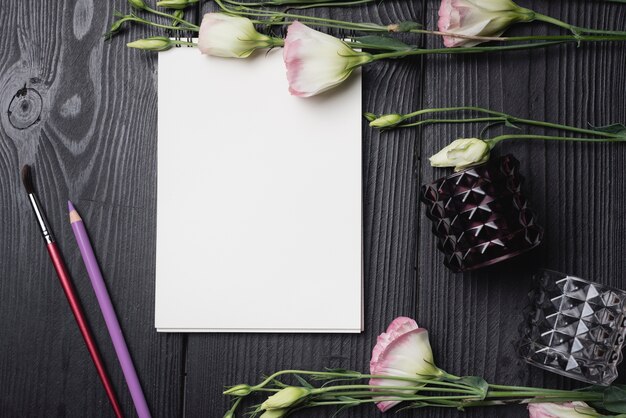 木製の黒い机の上に色鉛筆とブラシと白い白紙と新鮮な花
