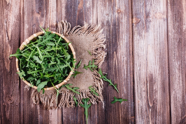 Свежие продукты, здоровый образ жизни. Зеленая руккола подается в миске на деревенском фоне
