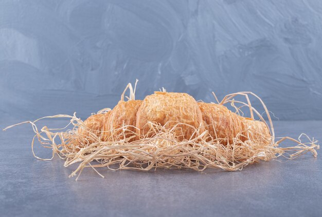 Fresh French croissant on straw over grey background.