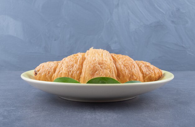 Fresh French croissant on white plate over grey background.