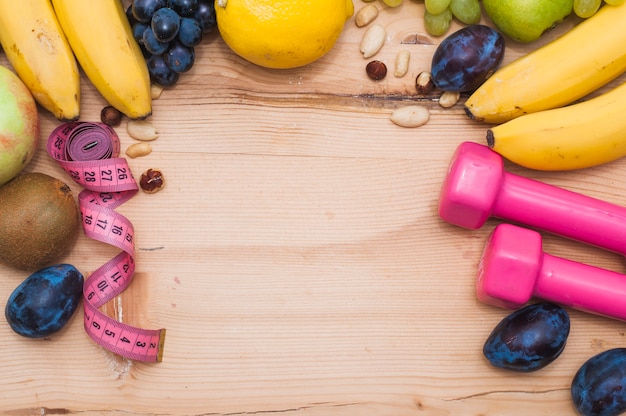 Fresh fruits; dry fruits; measuring tape and pink dumbbells on wooden table