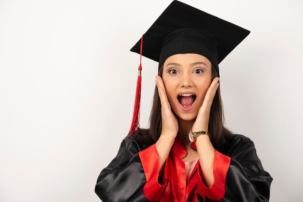 Fresh graduate covering her ears with surprised expression on white background.