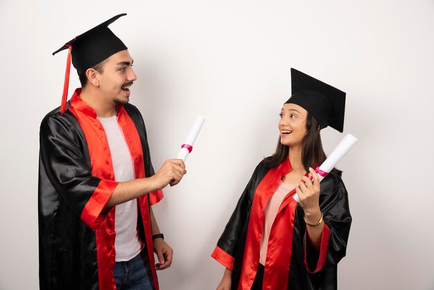 Fresh graduates in gown posing with diploma on white.