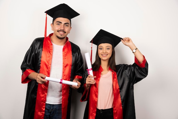 Fresh graduates in gown posing with diploma on white.