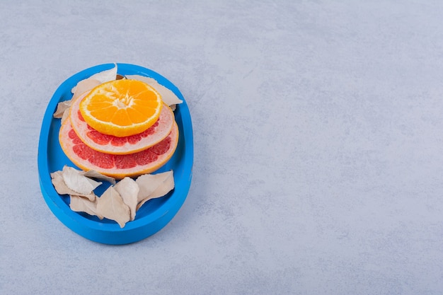 Fresh grapefruit, lemon and orange rings on blue plate. 