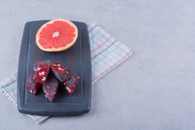 Fresh grapefruit slice and tasty oriental sweets on dark board.