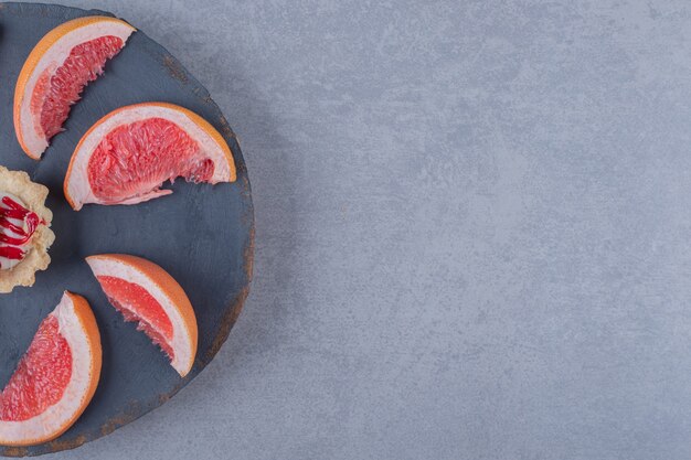 Ломтики свежего грейпфрута с печеньем на серой деревянной тарелке